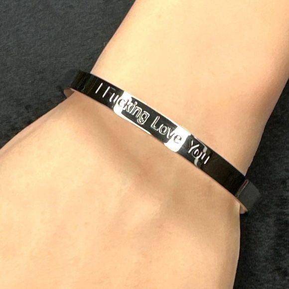 Black bracelet with 'I fucking love you' text on a wrist against a dark background
