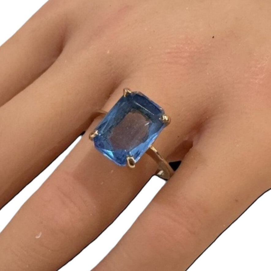Gold ring with a blue gemstone on a hand against a white background