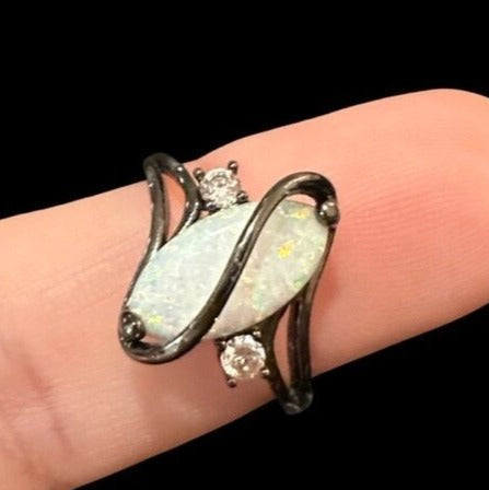 Ring with opal stone and diamonds on a finger against a black background