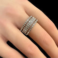 Silver ring with gemstones on a person's finger against a black background