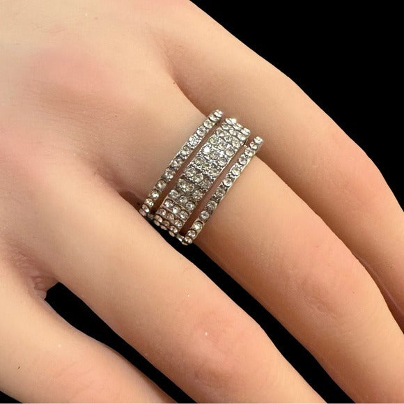 Silver ring with gemstones on a person's finger against a black background