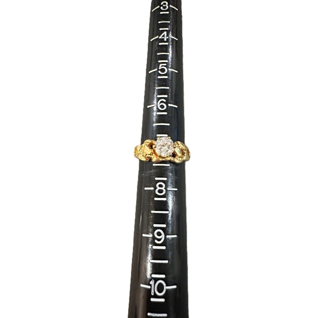 Gold ring with a diamond on a black cylindrical object with measurements.