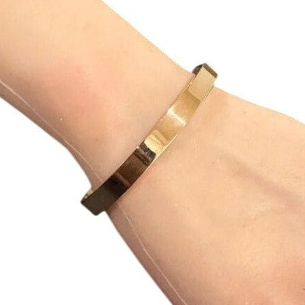 Gold bracelet on a wrist with a plain background