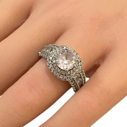 Silver ring with a large central gemstone on a person's finger against a white background