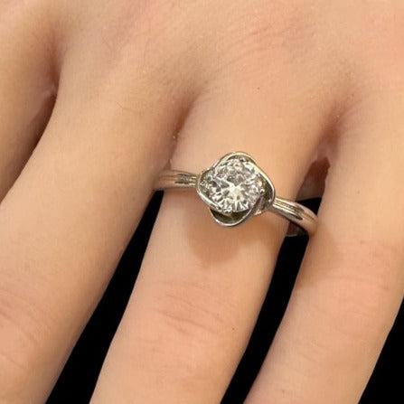 Silver ring with a diamond on a finger against a neutral background