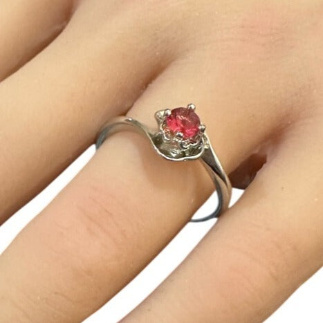 Silver ring with a red gemstone on a finger against a white background
