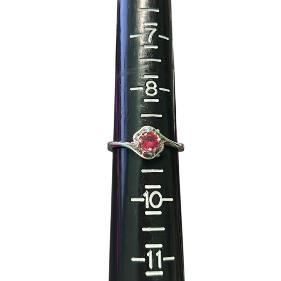 Ring with a red gemstone on a black cylindrical object with measurement markings.